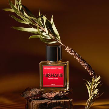Nishane Hundred Silent Ways perfume bottle on wood with botanical elements and warm shadows — luxury fragrance still life by Los Angeles product photographer