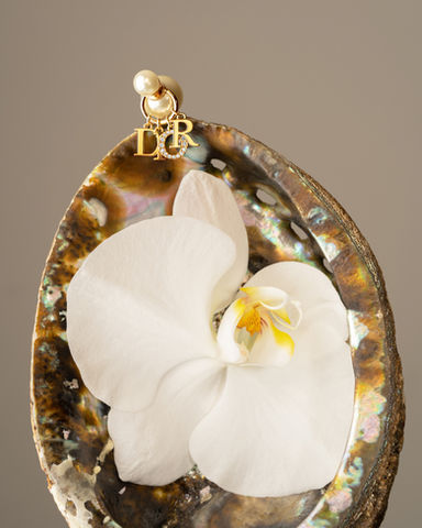 Dior pearl earring with gold logo styled on abalone shell and white orchid by Los Angeles jewelry product photographer