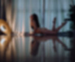 Woman in a yoga pose on a reflective floor, lit by soft yellow light. Curtains and plants in the background create a serene ambiance.