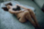 Woman in black lace lingerie lies on a gray shag rug, head tilted back, conveying relaxation. Soft lighting enhances the calm atmosphere.