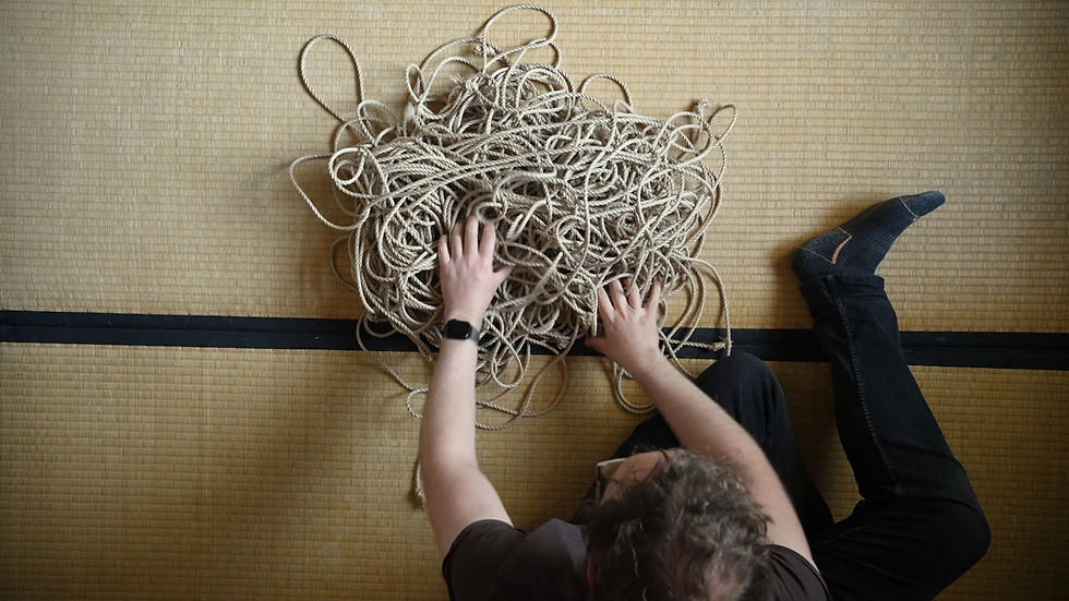 A tangled mess of jute rope is on the floor with someone untangling it.
