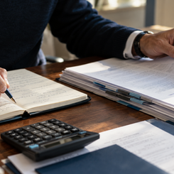 Manos revisando un expediente de resultados junto a una libreta y una calculadora.