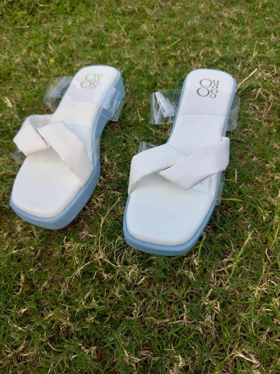 Pair of white sandals with blue soles, sitting on green grass background.