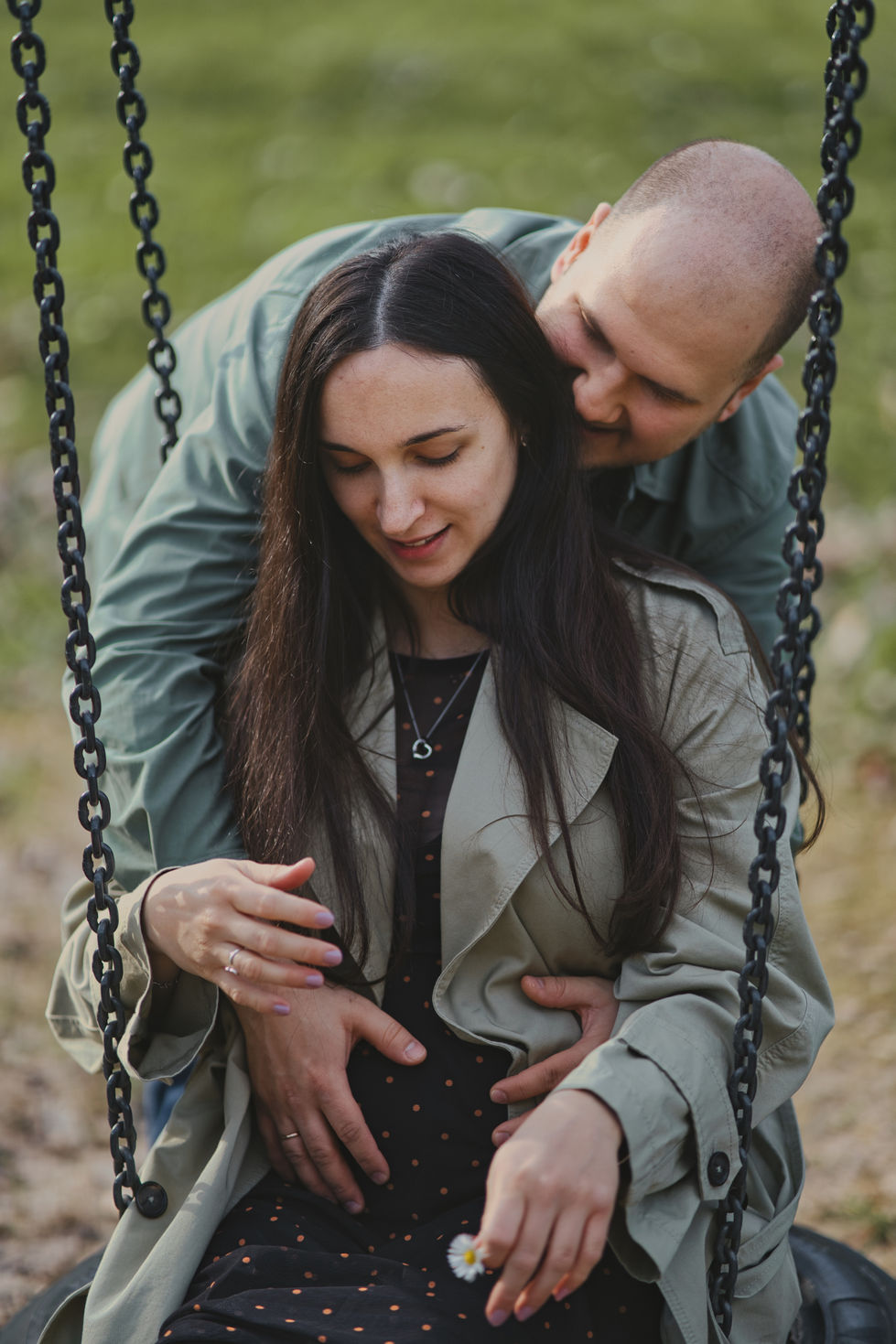 Familien Shooting - Mutter und Vater auf der Schaukel während sie den Babybauch halten