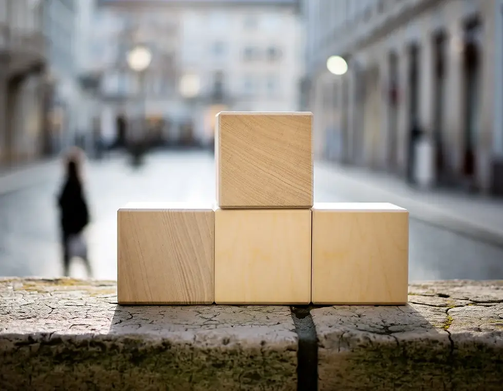 Four clean wooden blocks stacked on a stone ledge with a blurred passerby, supporting the section on factors that change costs.