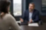 Attorney and client seated at a conference table with open hands and a closed case folder between them in a Salt Lake City law office
