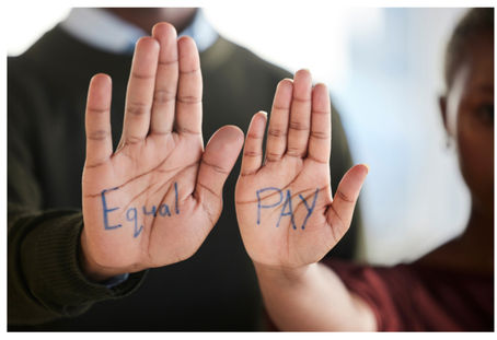 A girl and boy holding up their hands that have writing on them, together reading "equal pay".