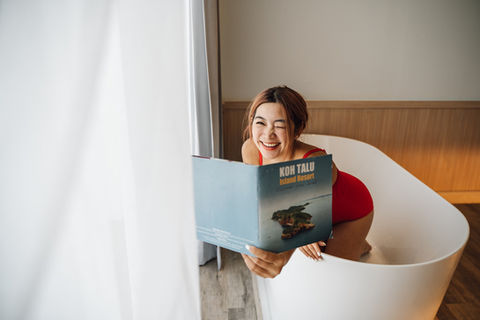 ผู้หญิงยิ้มในอ่างอาบน้ำ ถือหนังสือ 'เกาะทะลุรีสอร์ท'
