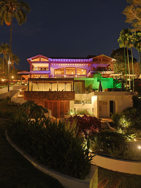 Illuminated tropical resort villa at night, framed by palm trees and lush gardens under a dark sky.