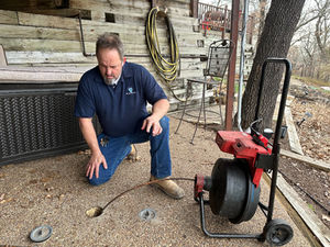Plumber kneeling outdoors while inspecting a main sewer cleanout with a professional drain cleaning machine