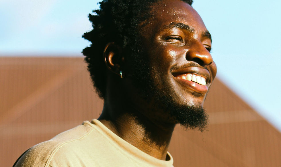 A young man smiling warmly outdoors in the sunlight