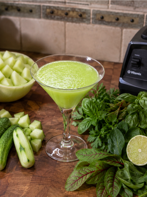 a glass of refreshing honeydew melon and cucumber gazpacho surrounded by the fresh ingredients
