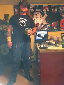 Man in black strip club choppers shirt, holding beer, at desk