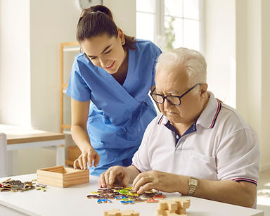 Friendly caregiver or nurse in the retirement home helping a senior man with puzzle games.