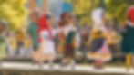 A parade of Capgrossos or people in costume walking over a wooden bridge next to water