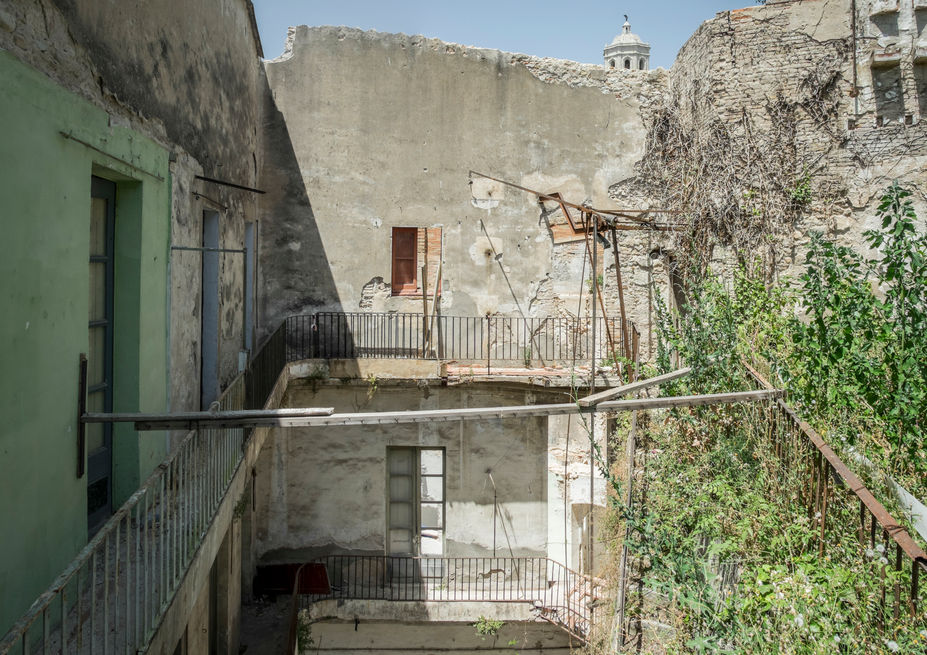 Run-down urban courtyard with crumbling buildings, balconies, and dense green foliage.