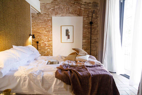 Large double bed with luxurious, rumpled sheets, stone wall detail in the background and doors opening onto a balcony