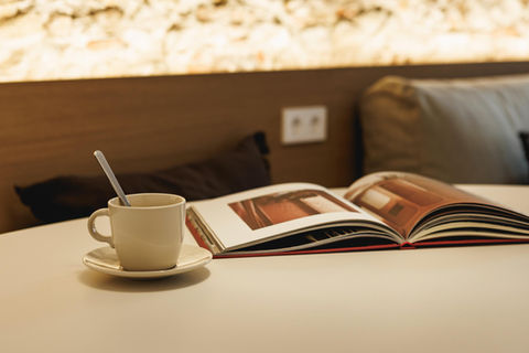 Coffee cup and open book on a table next to a bed