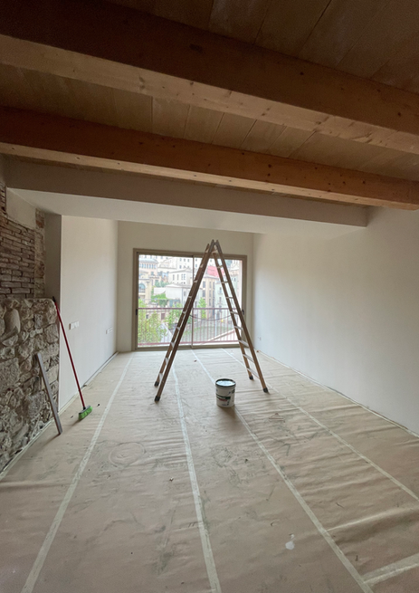 Room renovation in progress, ladder, paint can, covered floor, wood ceiling beams.