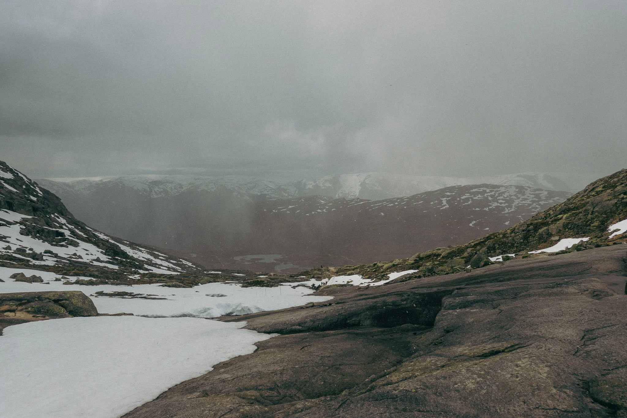 Dark cloudy skies and hailstorm forming with snow and rocks surrounding the Trolltunga trail in Norway