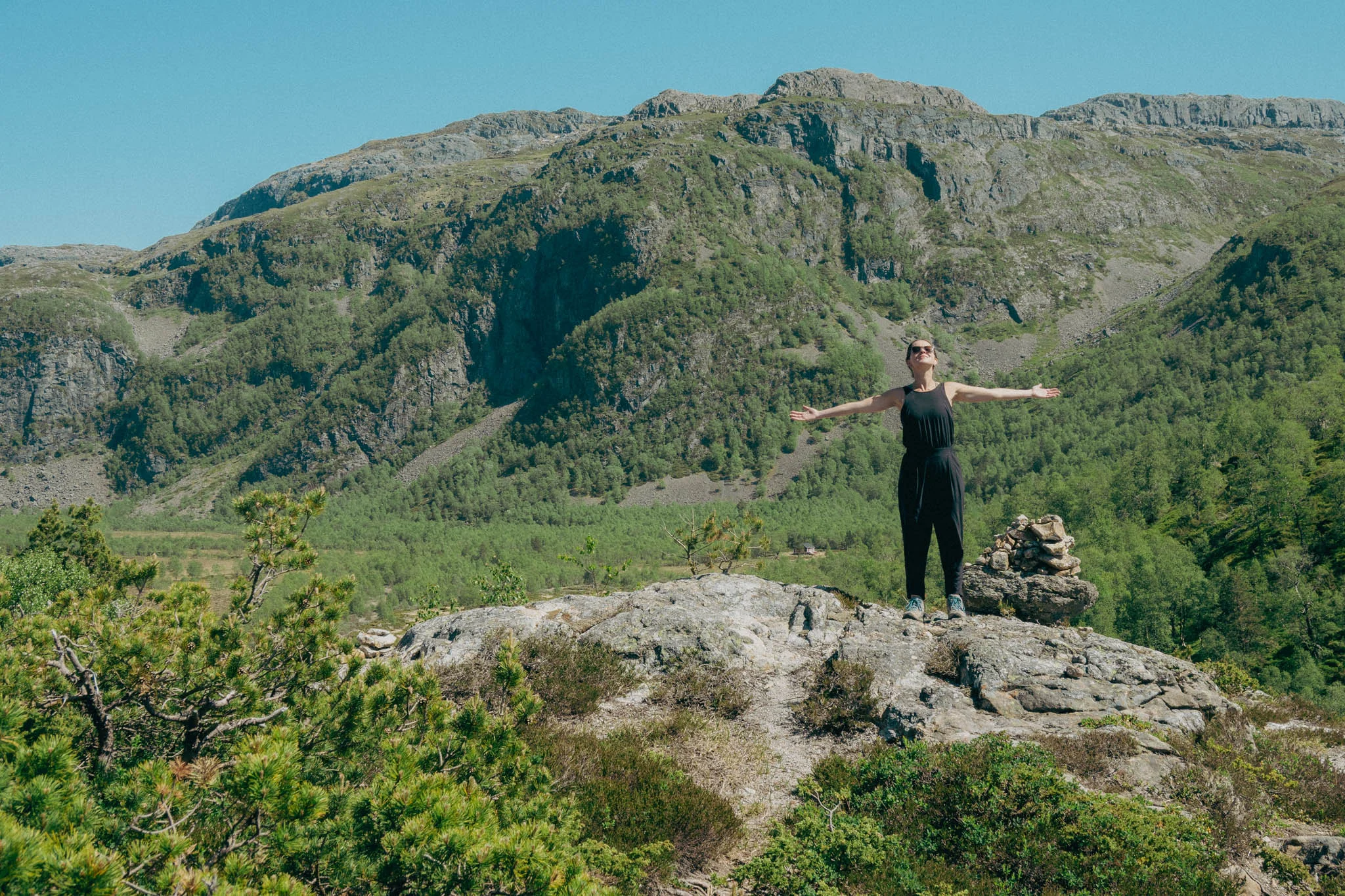 Woman standing on a rock with her arms spread wide taking in the view with mountains in the background.