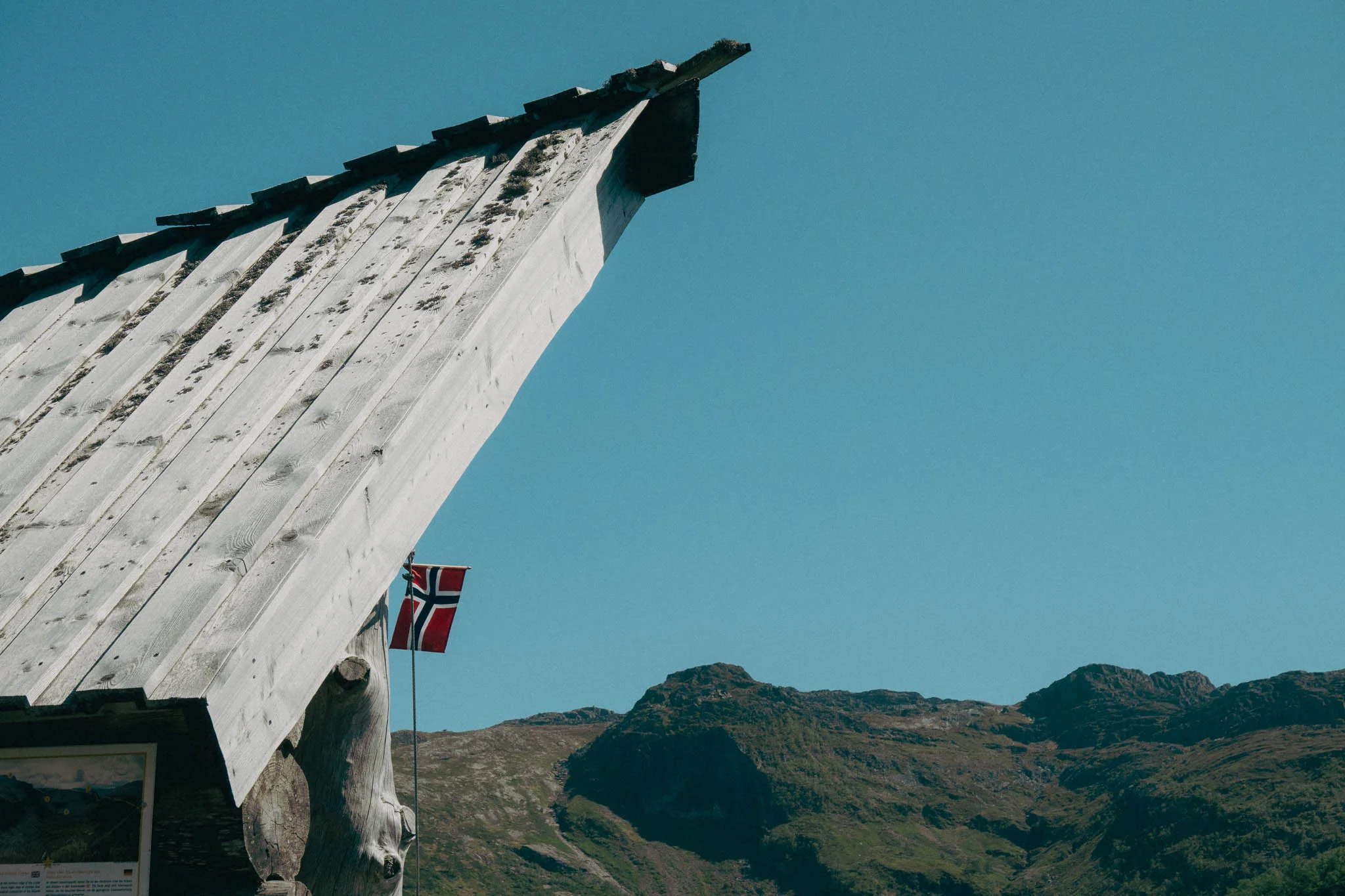 Wooden shelter roof and Norwegian flag in front of mountains at Ritland Crater in Norway