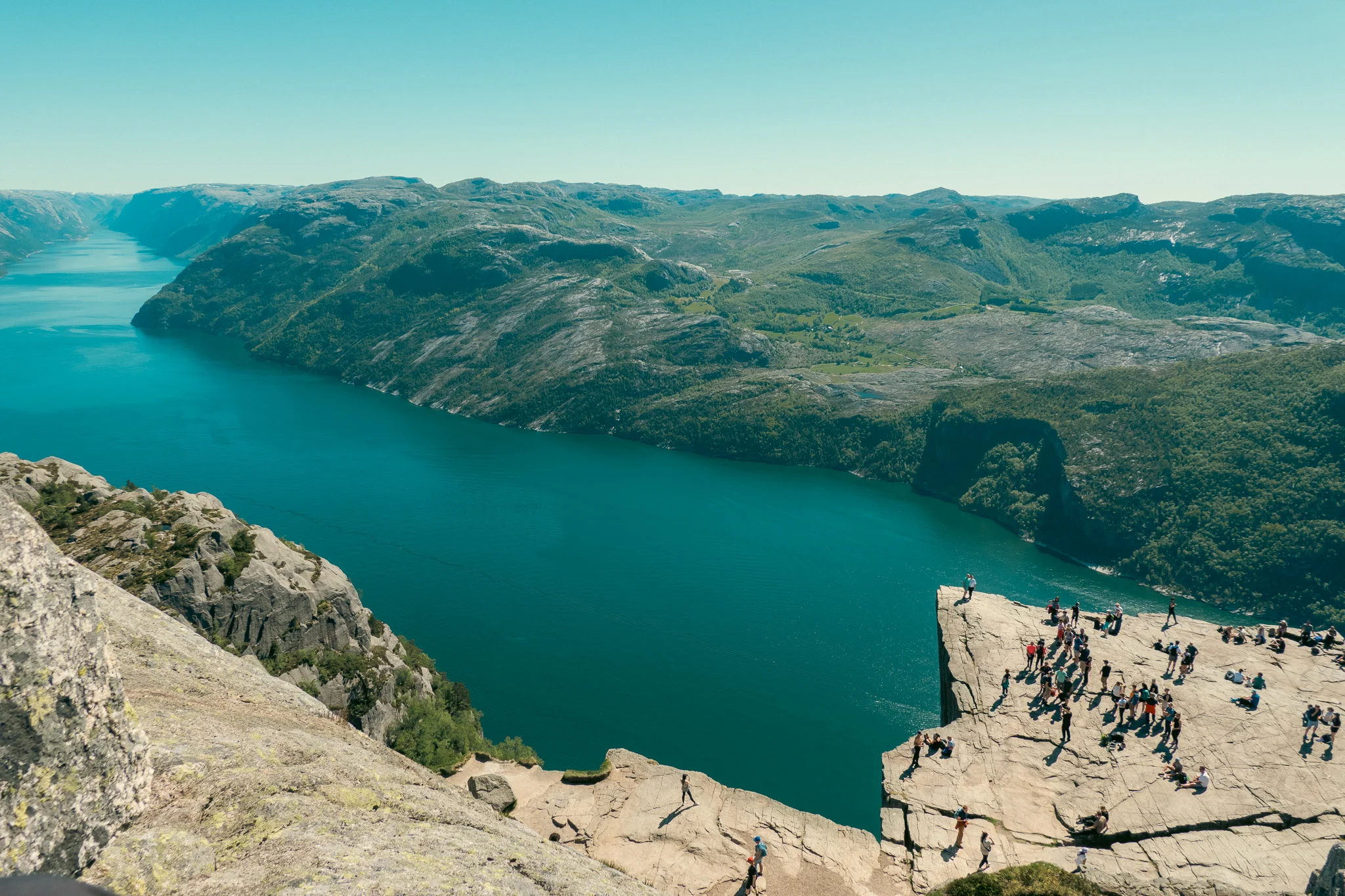 Groups of people on top of Pulpit Rock with the fjord and mountains in the background in Norway.