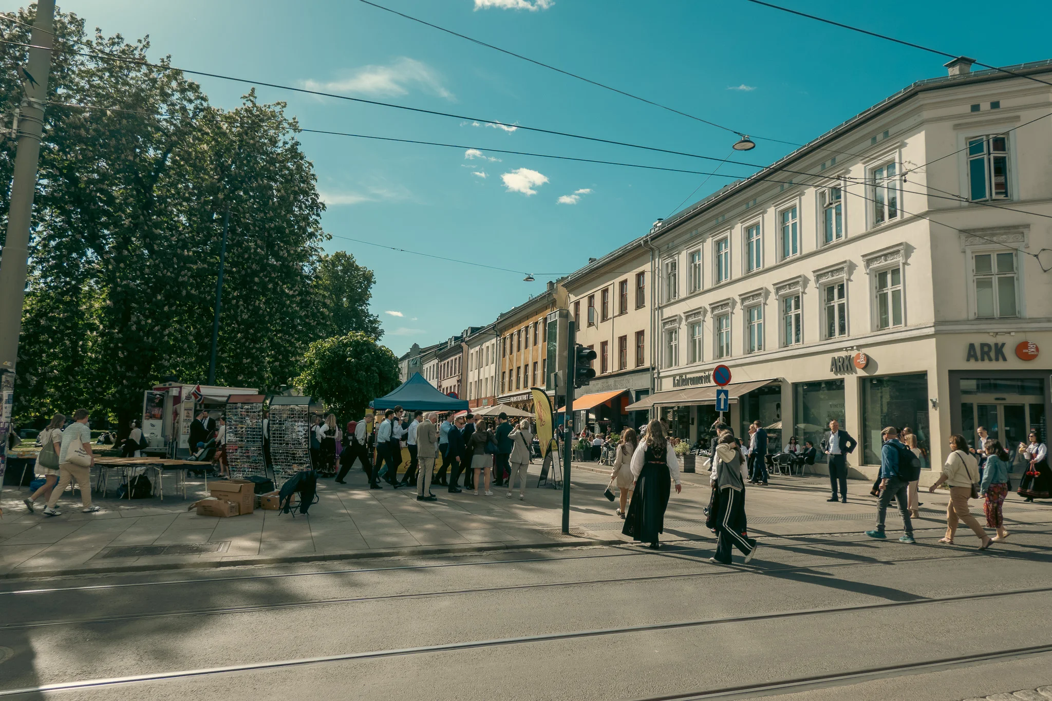 Blue skies, trees, and a bustling sidewalk in Oslo, Norway on Constitution Day.