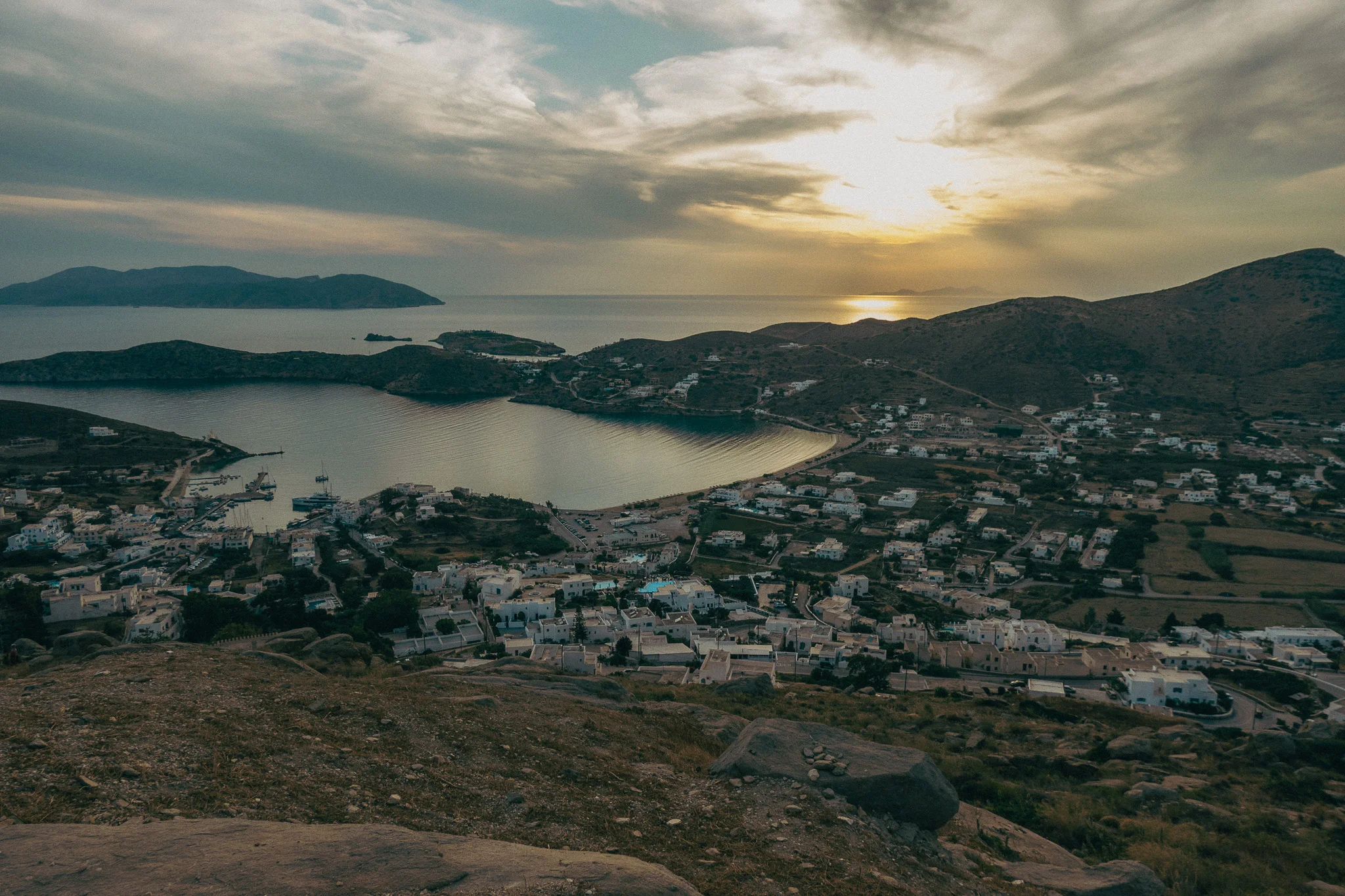Sunset over the mountains and water with white buildings and small shrubs in the foreground