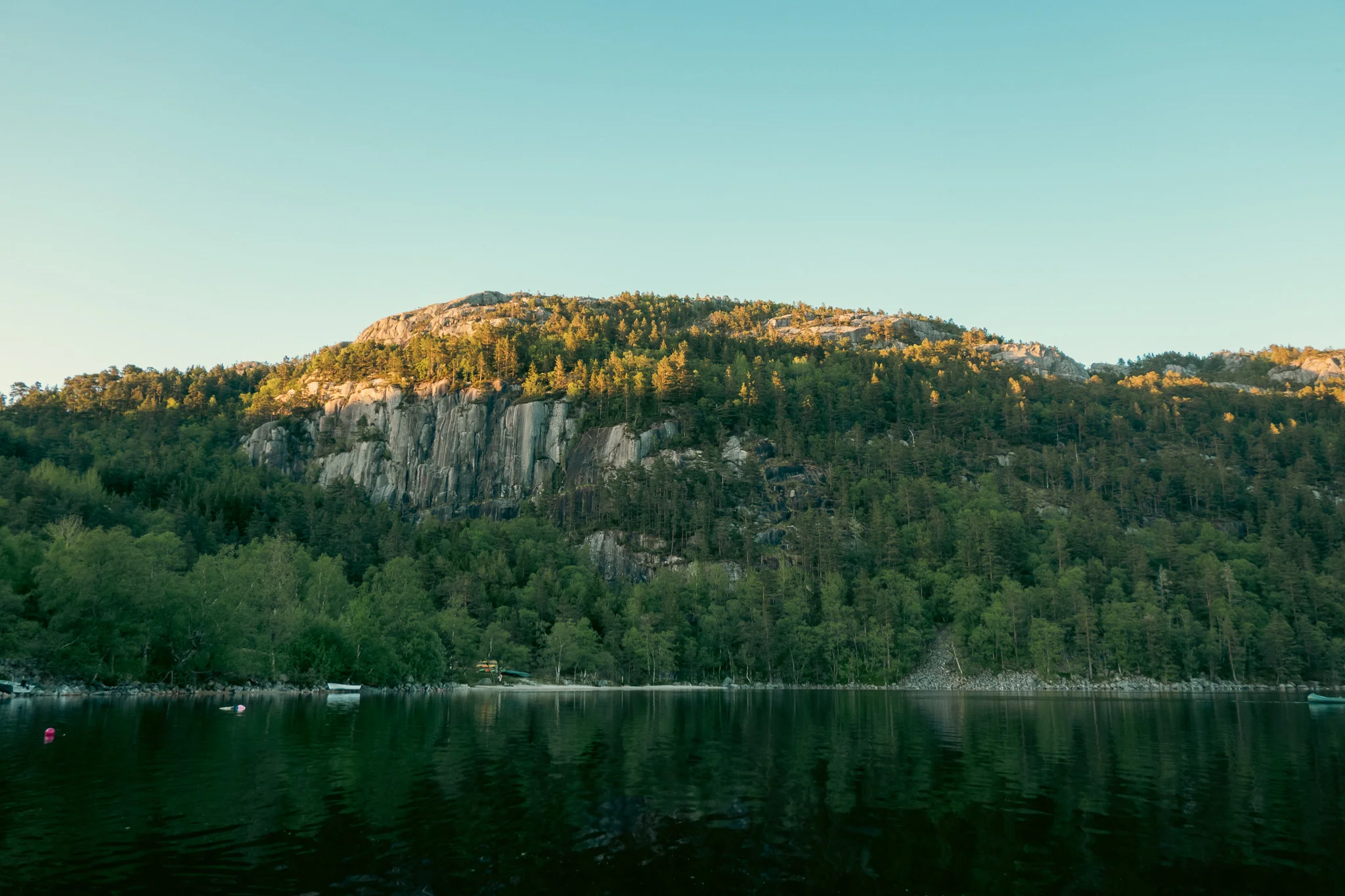 Tree-lined mountain alongside a lake at sunset.
