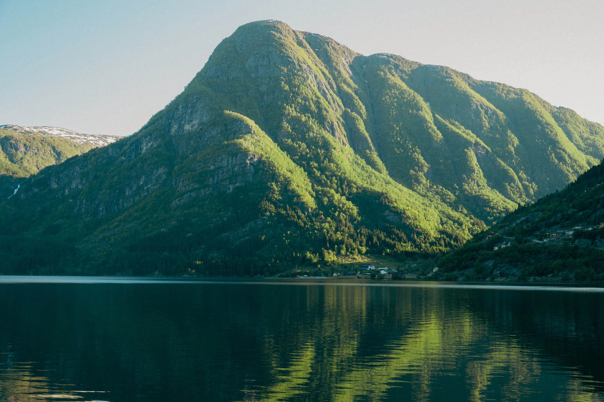 Clear fjord water reflecting the green sunlit mountains in the background