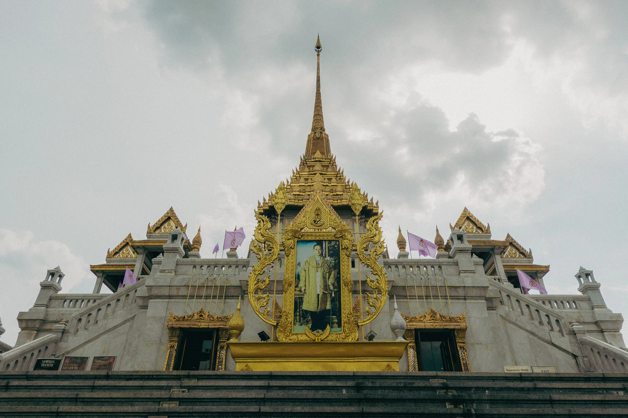 Large gold and white traditional Thai temple with stairs in the foreground and cloudy skies in the background