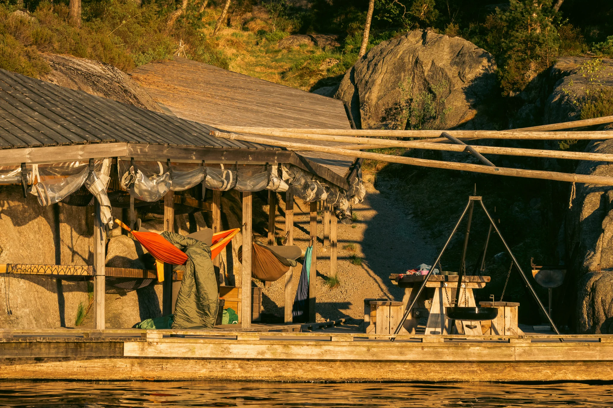 Preikestolen Basecamp Water Camp dock with hammocks hanging and a picnic table and fire pit along the water at sunset in Norway