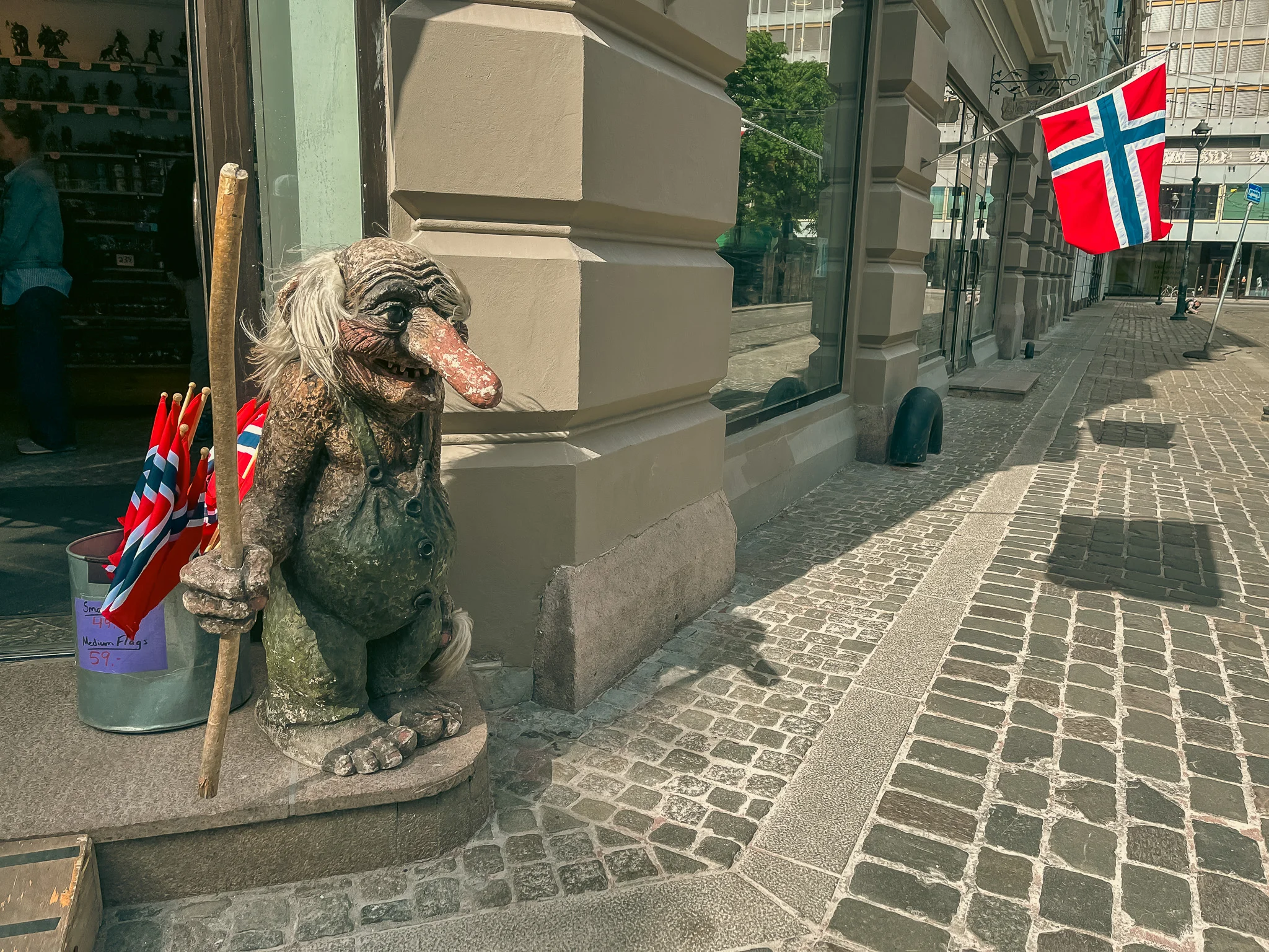 A statue of a troll outside a store on the sidewalk with the Norwegian flag in the background on Constitution Day in Oslo, Norway.