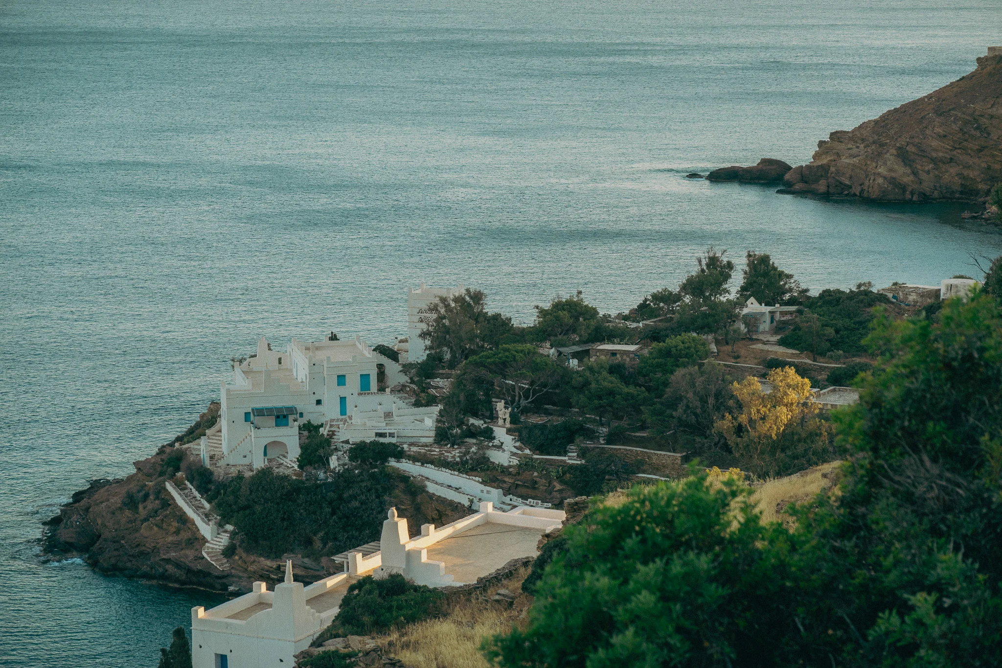 Two white buildings on the cliff overlooking the ocean surrounded by green trees and vegetation