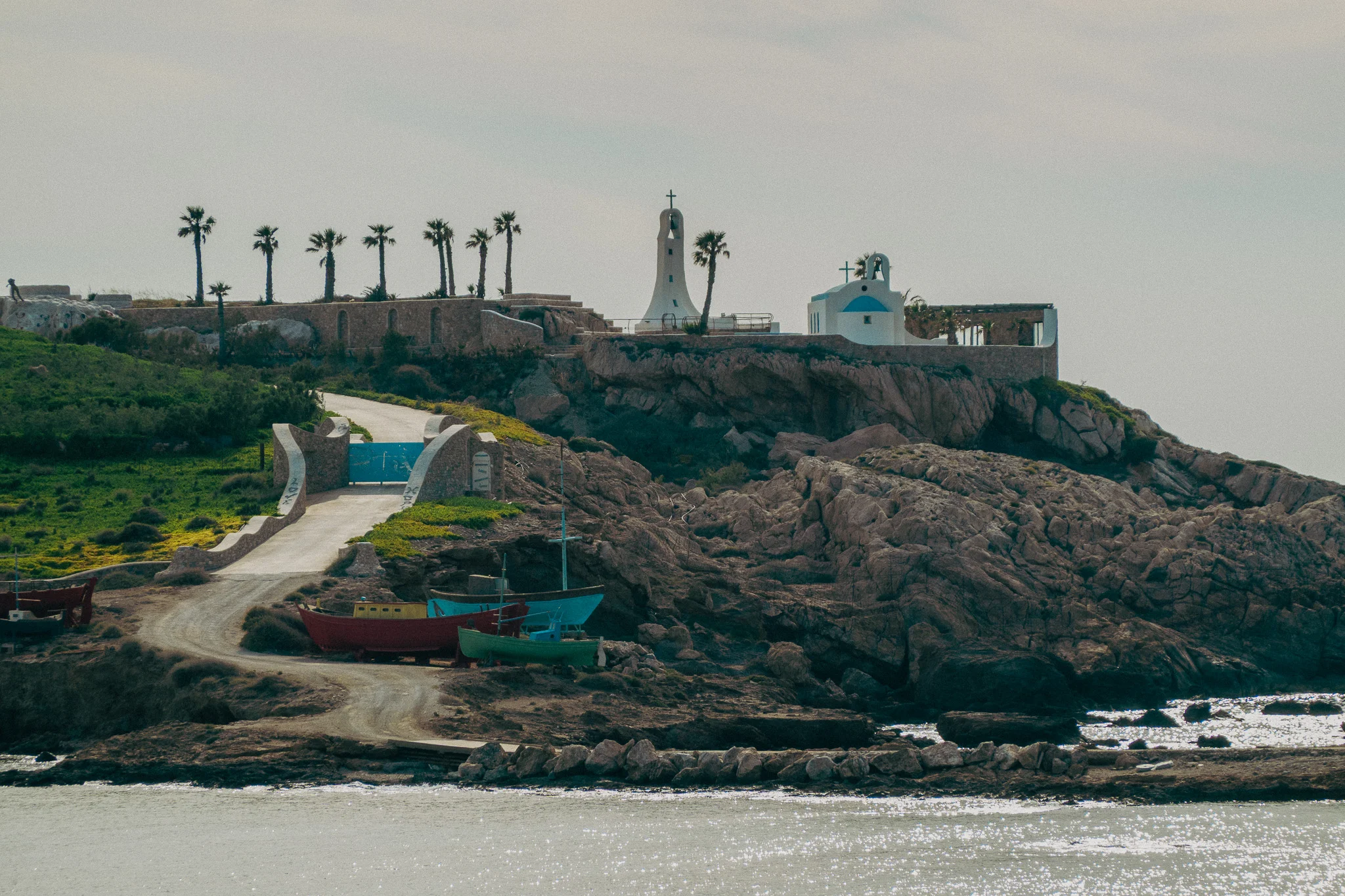 A road leads to an island with various buildings and palm trees