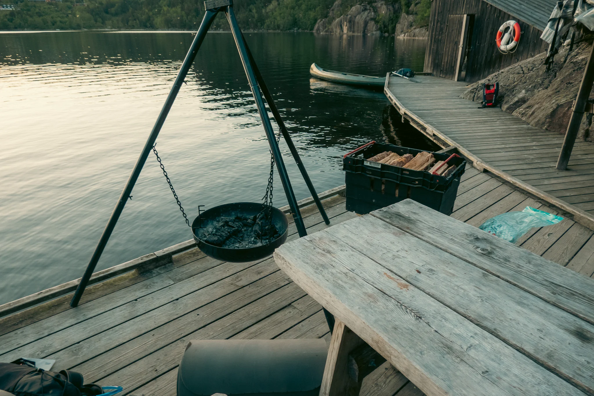 A picnic table and fire pit on a lakeside campsite with a canoe in the background.
