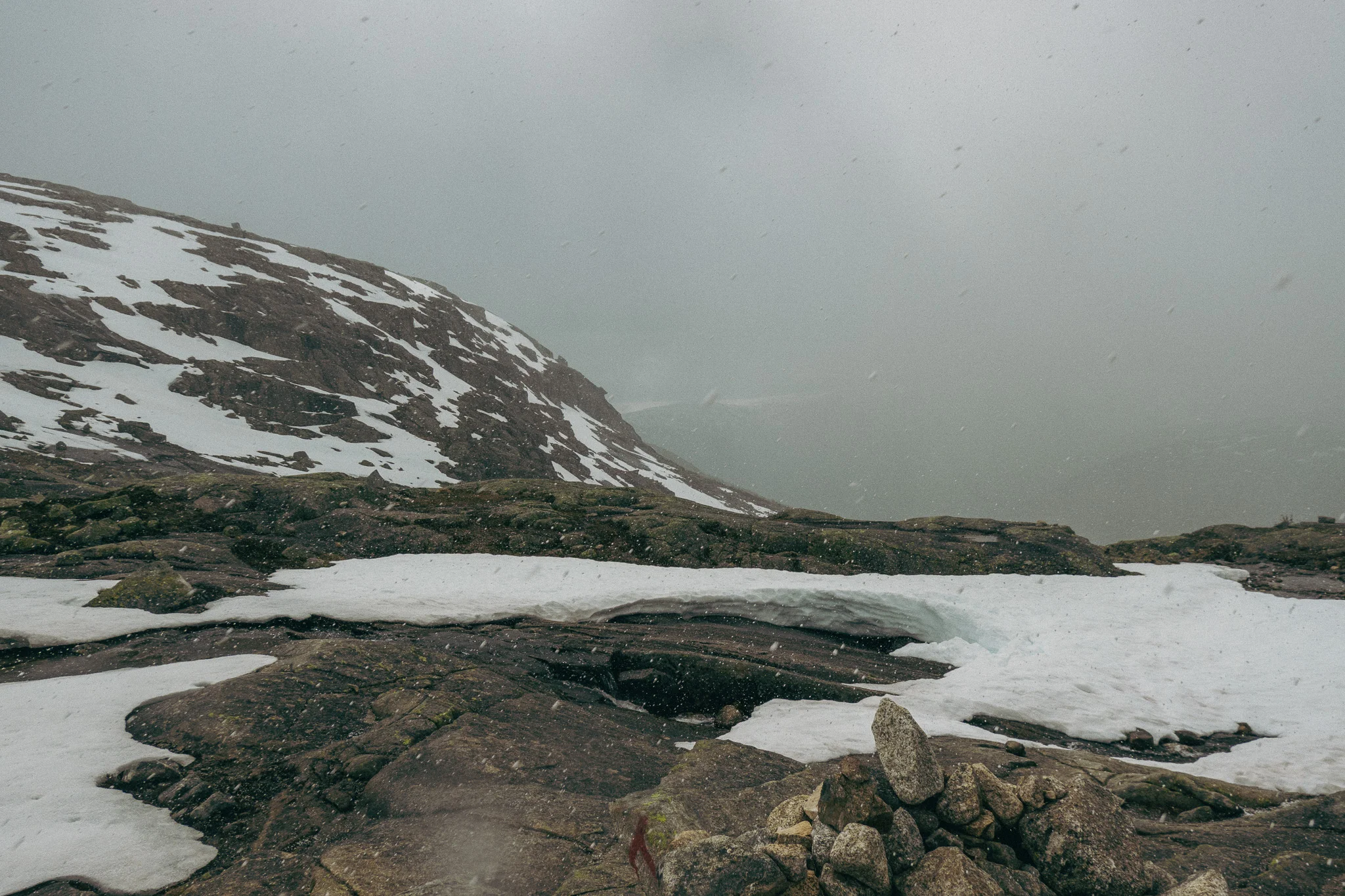 Dark cloudy skies and hailstorm forming with snow and rocks surrounding the Trolltunga trail in Norway