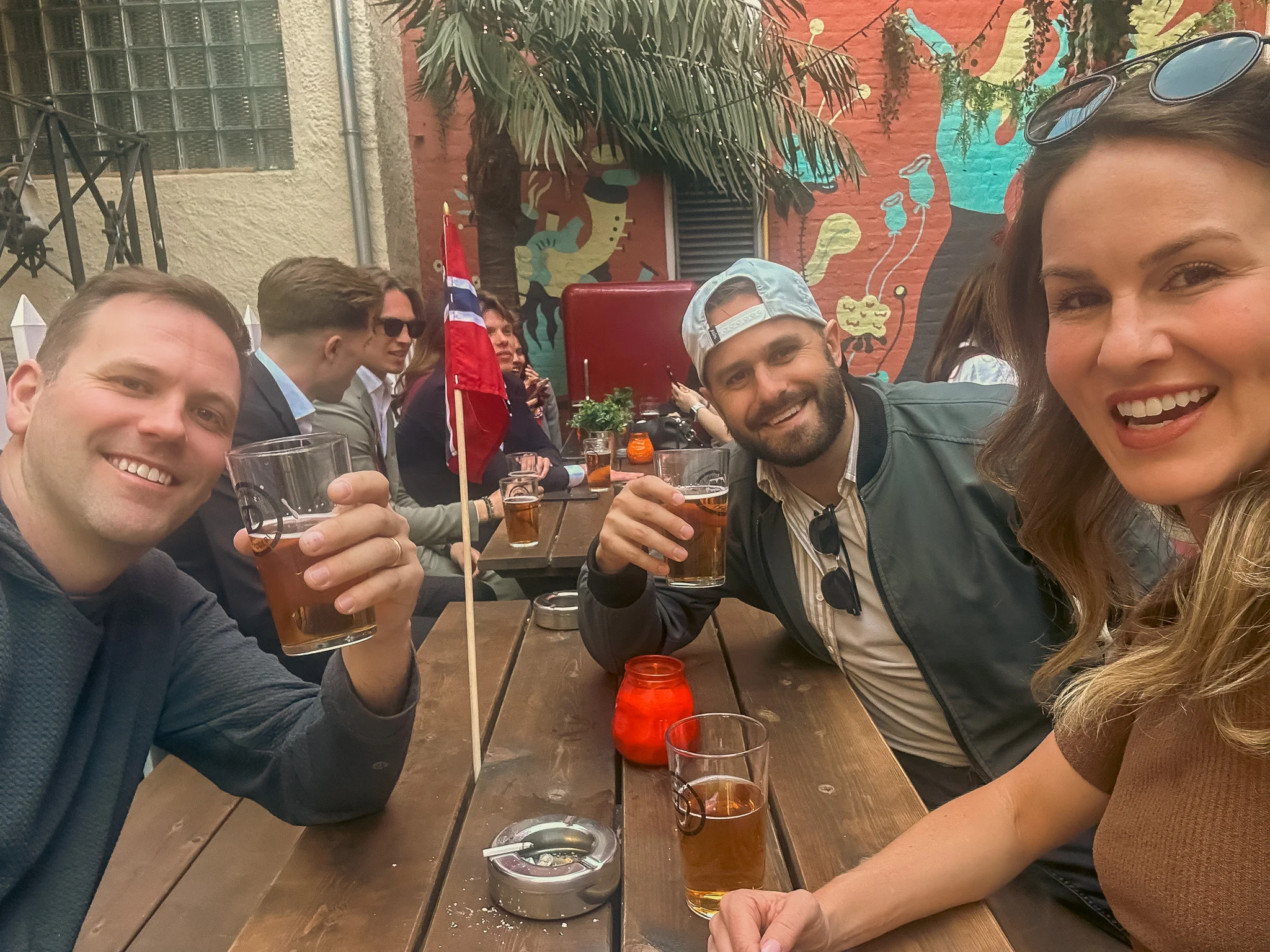Doug, Hunter, and Kelly toasting beers and taking a selfie on the back patio of Rebell bar celebrating Constitution Day in Oslo, Norway.