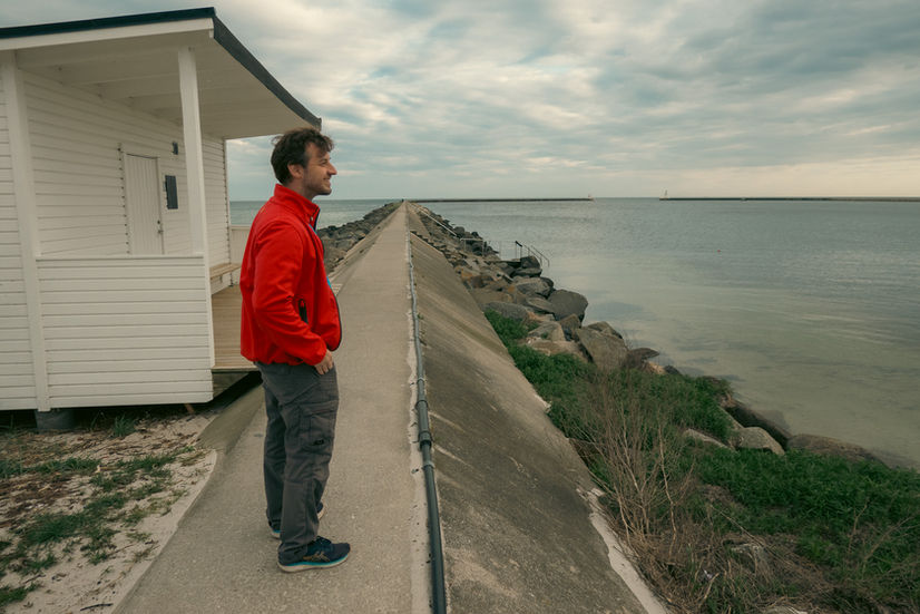 Alex in a red jacket looking out over the water from the breakwater walkway at Höllviken beach in Sweden