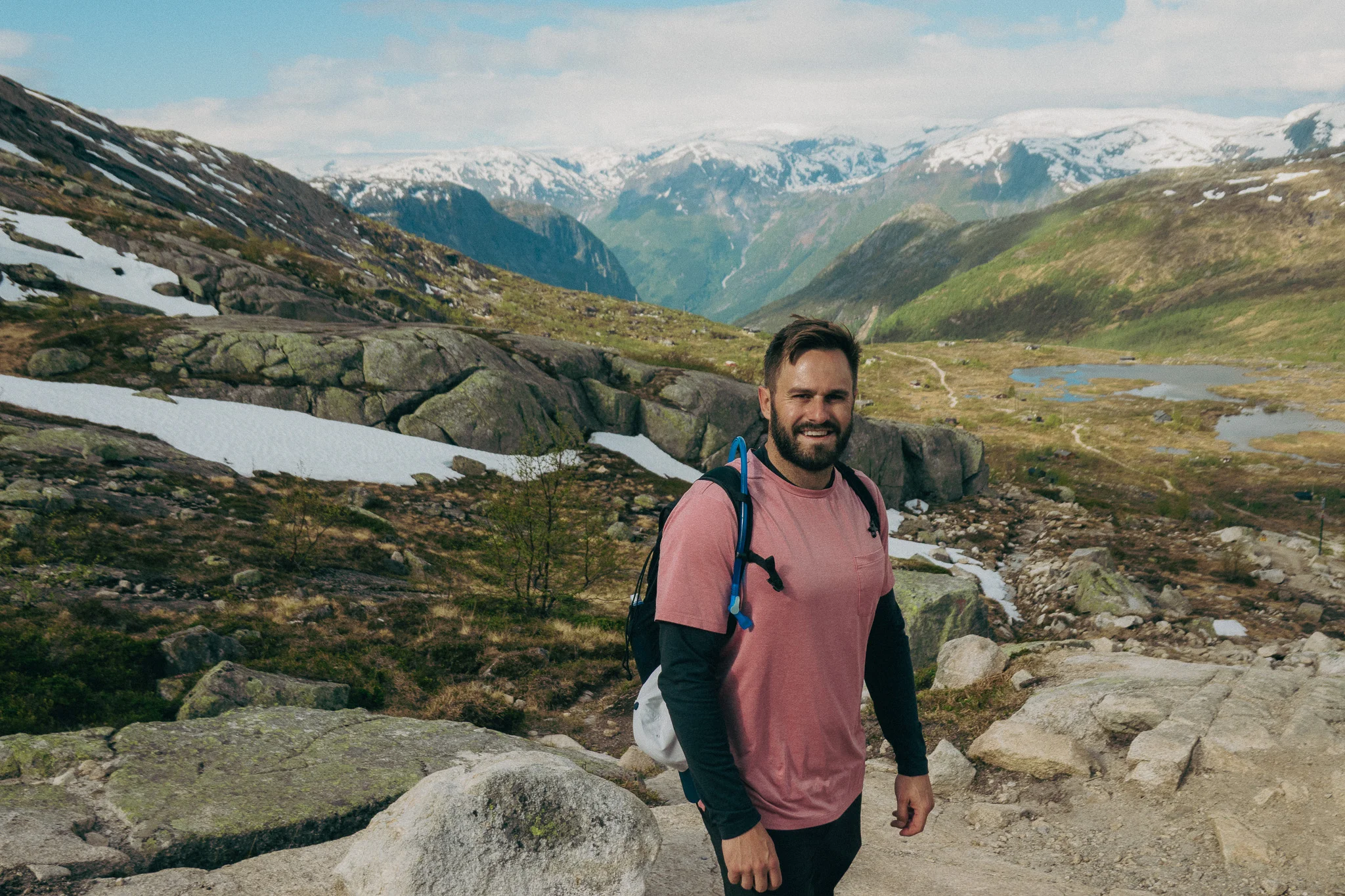 Adult male poses in front of scenic landscape and snowcapped mountains on the Trolltunga trail in Norway