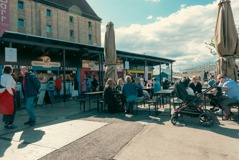 People eating at picnic tables in front of a food stand at Broens Street Food in Copenhagen, Denmark