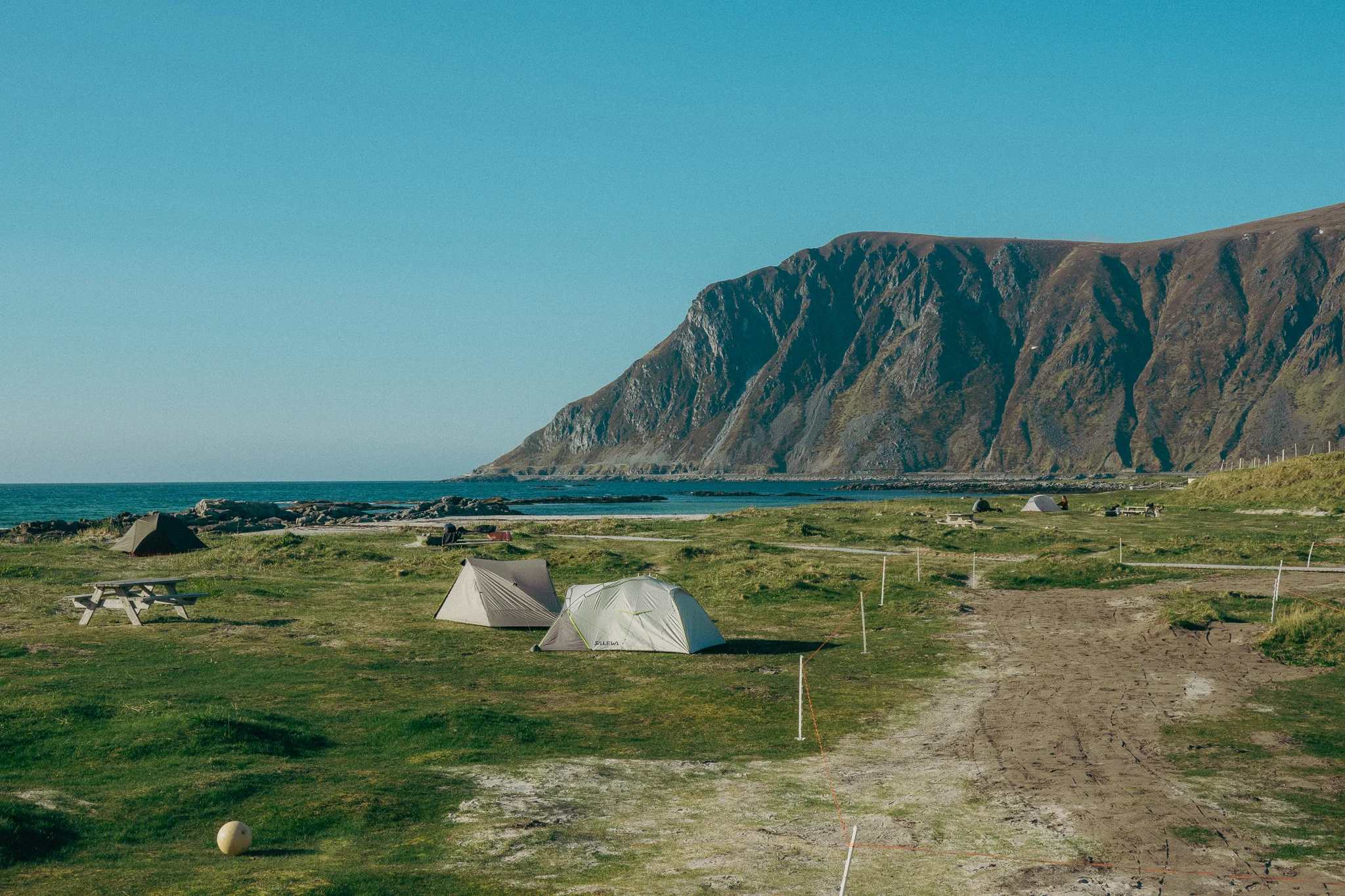 White tents pitched on a beachside campground with mountains in the background
