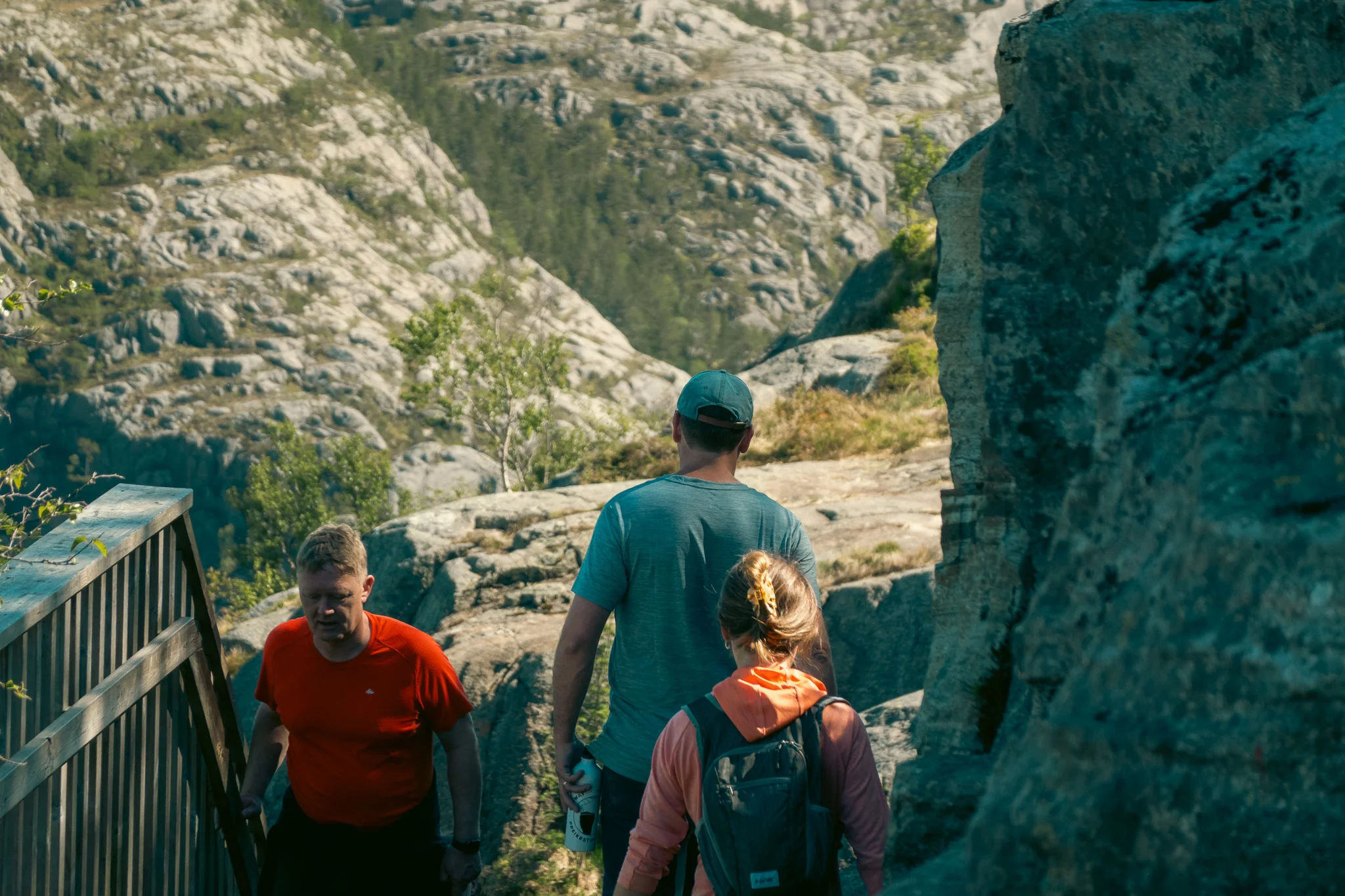 A man and woman walk along a rocky hiking trail with trees and mountains in the background giving a sense of adventure.