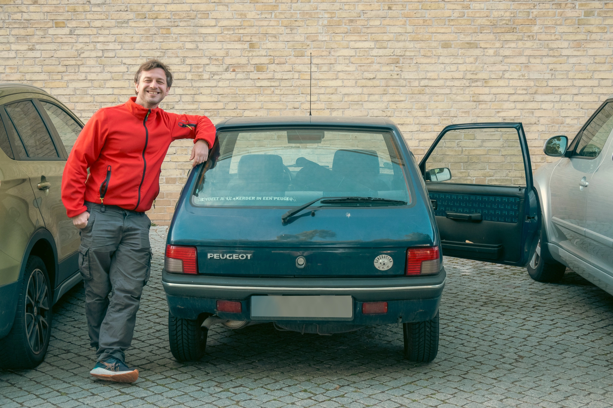 Alex in a red jacket standing in next to the 1996 Peugeot to his
