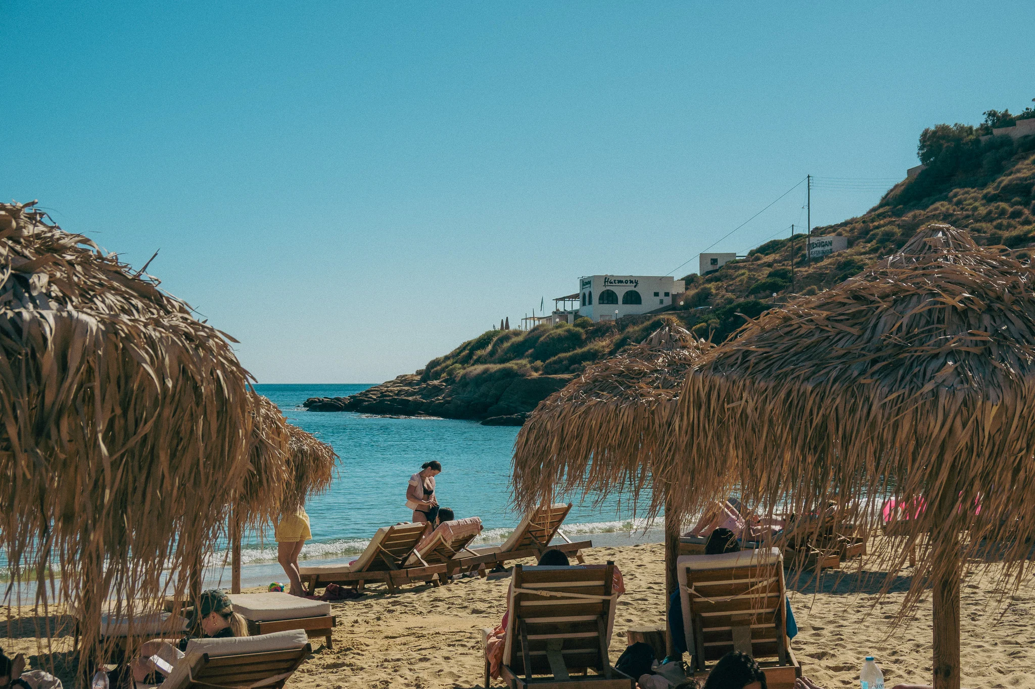 Beach chairs and straw umbrellas with ocean and a house on the cliff overlooking the water