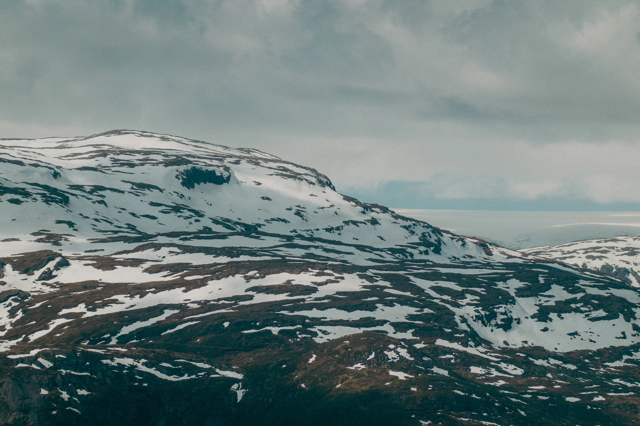Snowcapped mountains and cloudy grey skies on the Trolltunga trail in Norway