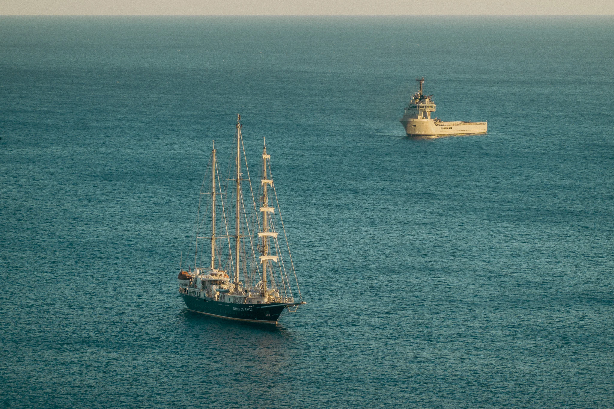 A tall sailing ship and cargo ship on the water