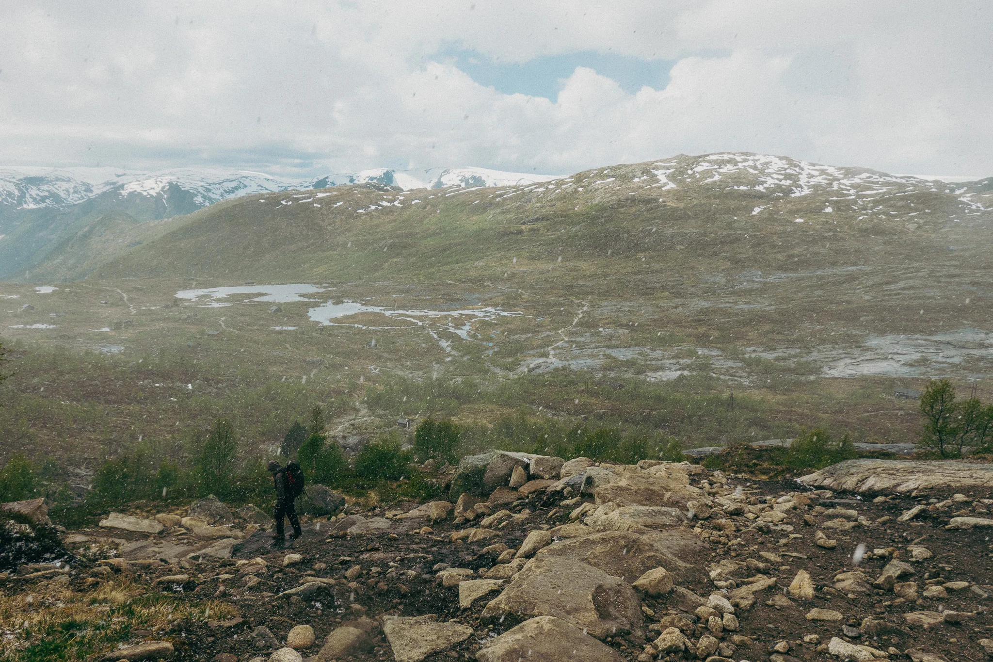 Dark cloudy skies and hailstorm forming with snow and rocks surrounding the Trolltunga trail in Norway