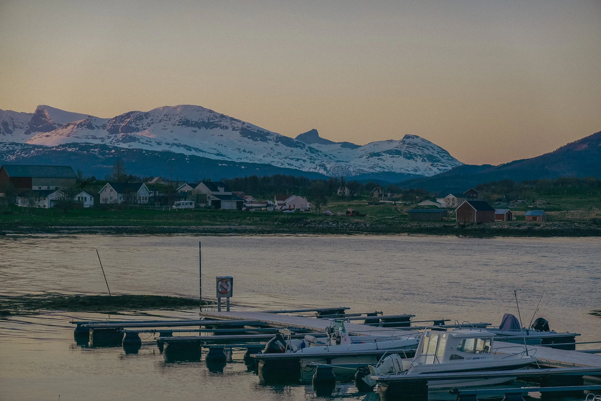 Snow-capped mountain landscape with water and rocky land and docked boats in the foreground at dusk in Narvick Norway